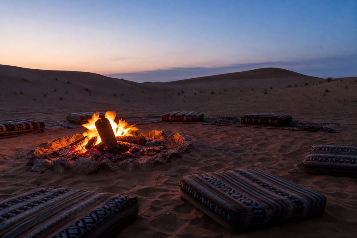 Travellers gathered around a fire at a desert camp with dunes fading into the dark in Wahiba Sands